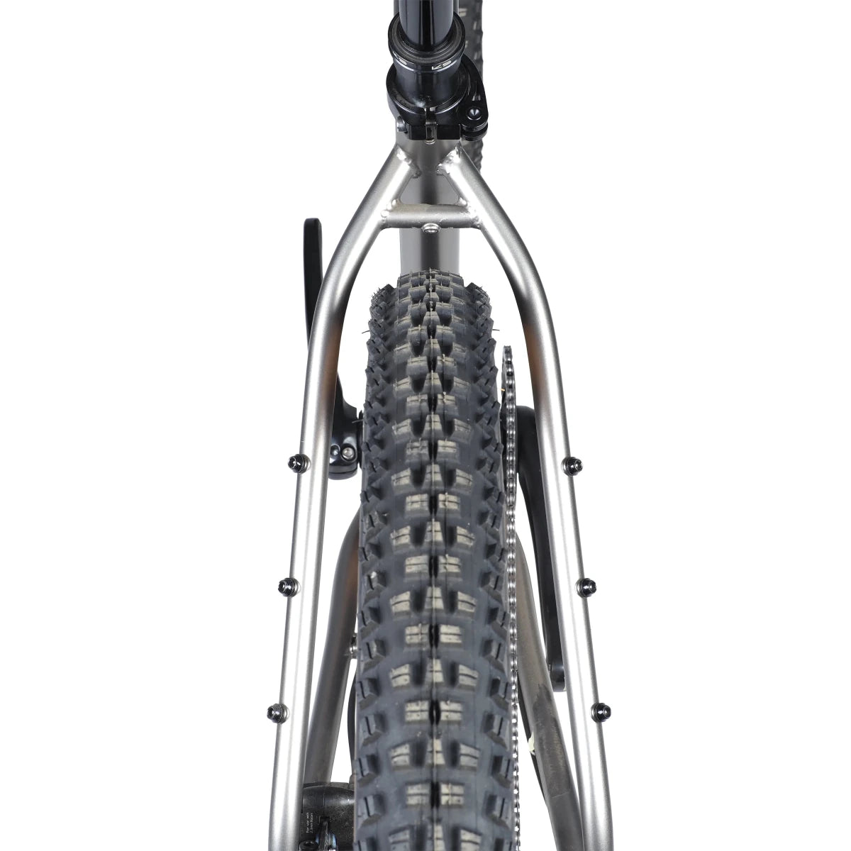 Breezer Thunder rear tire and stay clearance – Rear view of a knobby mountain bike tire fitted between raw steel seatstays featuring multiple threaded gear eyelets against a clean white background.