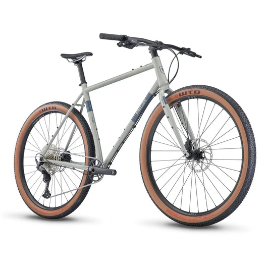 Breezer Radar Sport adventure gravel bicycle – A light grey steel-frame adventure bicycle with flat handlebars, black components, and knobby tan-wall WTB tires, shown from a three-quarters angle against a white background.