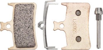 Hope E4 sintered brake pads pair – Two gold-toned metallic brake pads, shown front and back, alongside a silver retention spring clip and threaded retaining pin against a plain white backdrop.
