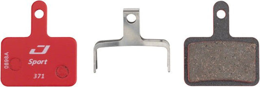 Jagwire Sport semi-metallic disc brake pads – Pair of bicycle disc brake pads showing the red branded backing plate, silver metal retention spring, and dark textured friction surface against a plain white background.
