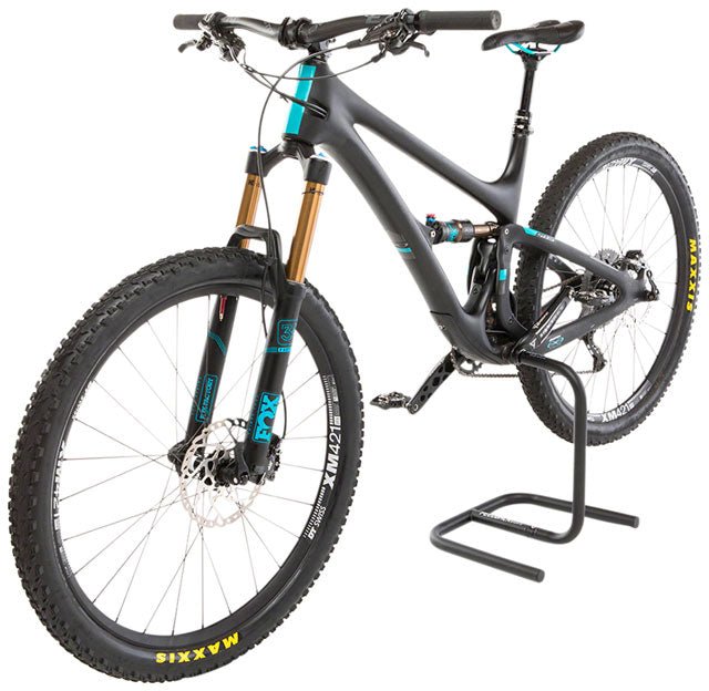 Feedback Sports Scorpion bike display stand – A matte black full-suspension mountain bike is elevated by a black tubular steel Scorpion display stand inserted into its hollow crank spindle.