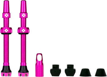 Pink Muc-Off V2 tubeless valve kit – Pair of bright pink anodized aluminum tubeless valves standing upright alongside an extra valve core tool cap and four black rubber grommets on white background.