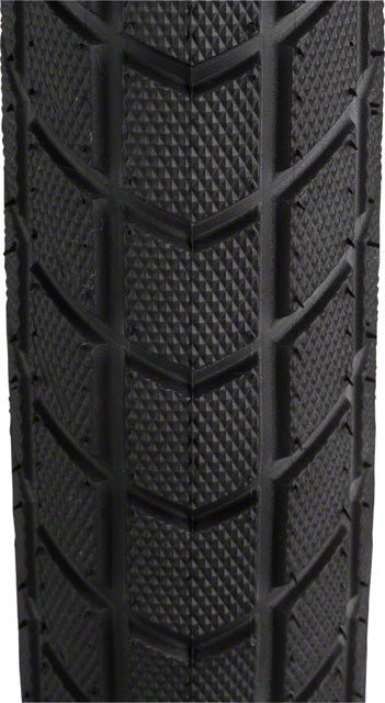 Schwalbe Super Moto-X bike tire tread – A close-up view shows the black rubber tread of a bicycle tire featuring a diamond knurled pattern between deep chevron-angled water evacuation grooves.