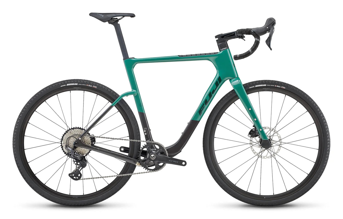 Fuji Jari Carbon 1.3 gravel bike – This green and dark grey gravel bike is shown from the side against a white background, featuring drop handlebars, disc brakes, and knobby off-road tires.