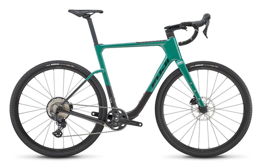Fuji Jari Carbon 1.3 gravel bike – This green and dark grey gravel bike is shown from the side against a white background, featuring drop handlebars, disc brakes, and knobby off-road tires.