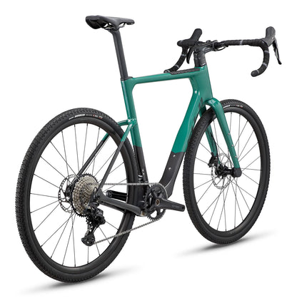 Fuji Jari Carbon teal gravel bike – Teal and matte black carbon gravel bicycle shown from a rear three-quarter angle on a white background, featuring drop handlebars, knobby tires, and disc brakes.