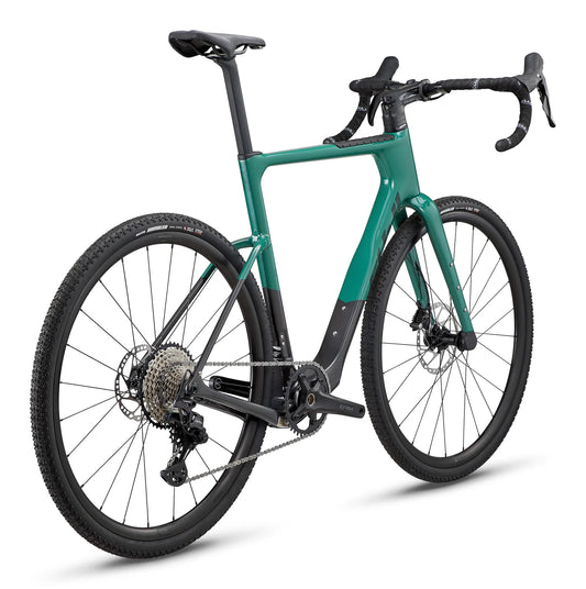 Fuji Jari Carbon teal gravel bike – Teal and matte black carbon gravel bicycle shown from a rear three-quarter angle on a white background, featuring drop handlebars, knobby tires, and disc brakes.