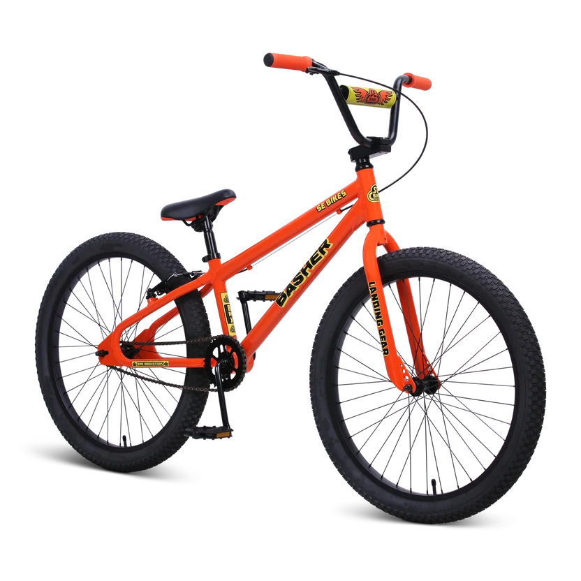 Orange SE Basher 24-inch BMX cruiser bike – Bright orange 24-inch BMX cruiser with black rims, knobby tires, high-rise handlebars with a yellow pad, and matching orange grips, displayed against a solid white background.