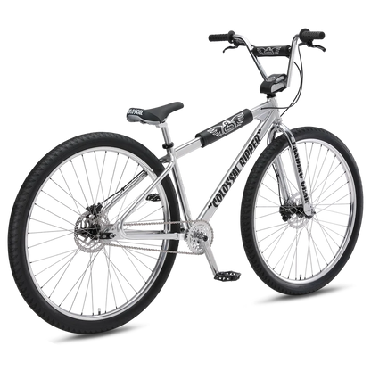 SE Colossal Ripper 32 silver BMX bike – A polished chrome-silver BMX cruiser bike stands on a white background, featuring large 32-inch black knobby tires, dual disc brakes, and retro black frame pads.