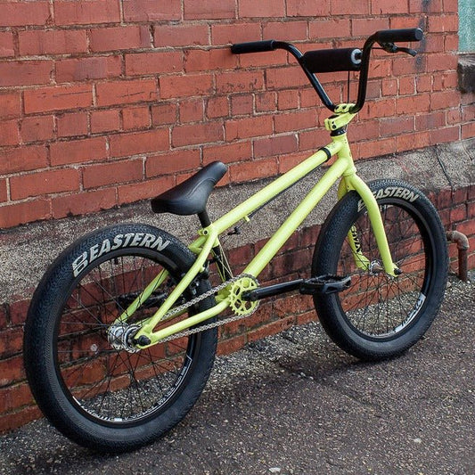Eastern Nightwasp 20-inch yellow BMX bike – A light yellow Eastern Nightwasp BMX bike leans against a weathered red brick wall, showcasing thick black Eastern-branded tires, black handlebars, and a low-profile saddle.