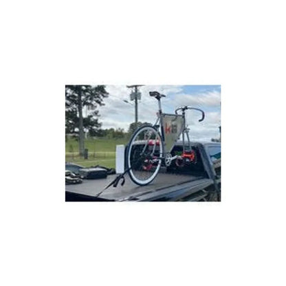 Kupper Mount bike rack on truck bed cover – A single road bicycle secured upright with a suction bike mount rack atop the black tonneau cover of a pickup truck bed outdoors.