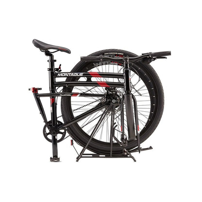 Montague Allston folding bike folded position – A matte black Montague Allston folding bike stands collapsed against a white background, showing its folded frame with red graphics, belt-drive system, and rear wheel.